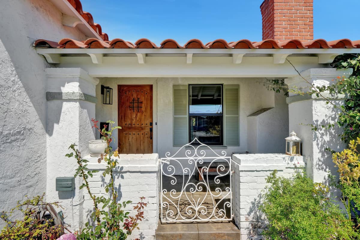 The Spanish-style front of the home, with a white brick wall, arched wooden door and garden flowers