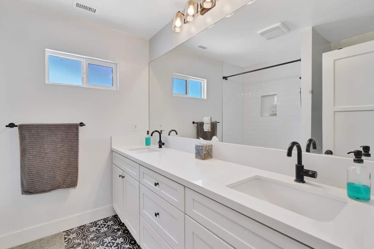 The bathroom with a white double vanity, mirror and shower