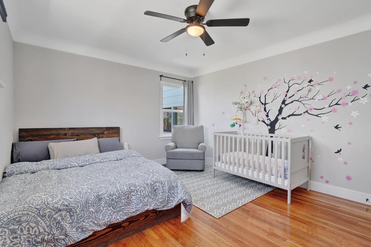 The second bedroom with a Queen bed, a crib and a cherry-blossom wall mural