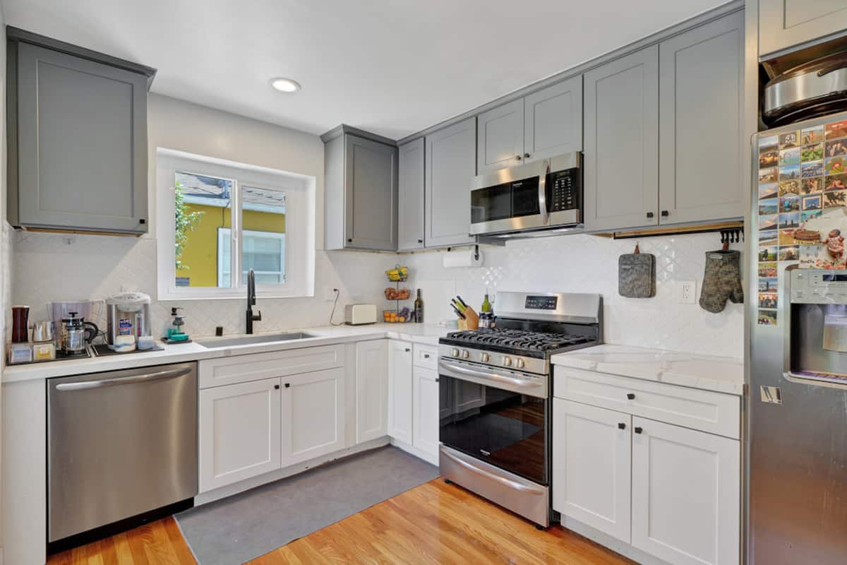 The full kitchen with white cabinets, gas stove and stainless appliances